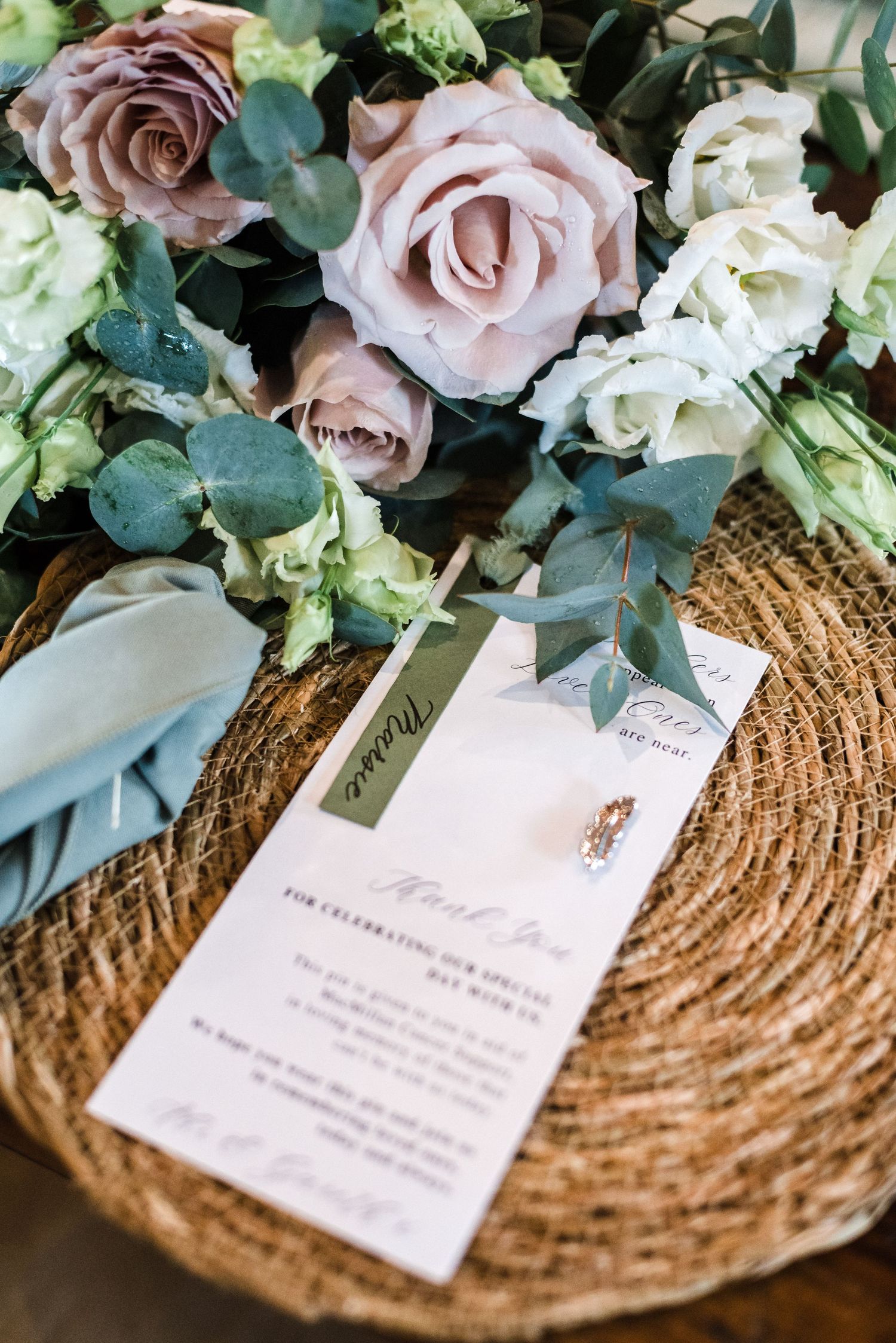 Wedding invitation card with dusty pink roses and eucalyptus on woven charger plate.