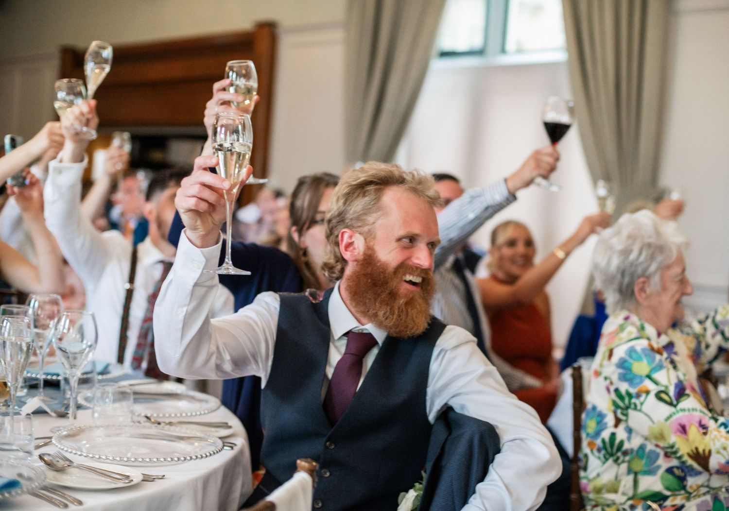 Wedding guests on dance floor laugh and celebrate during reception party.