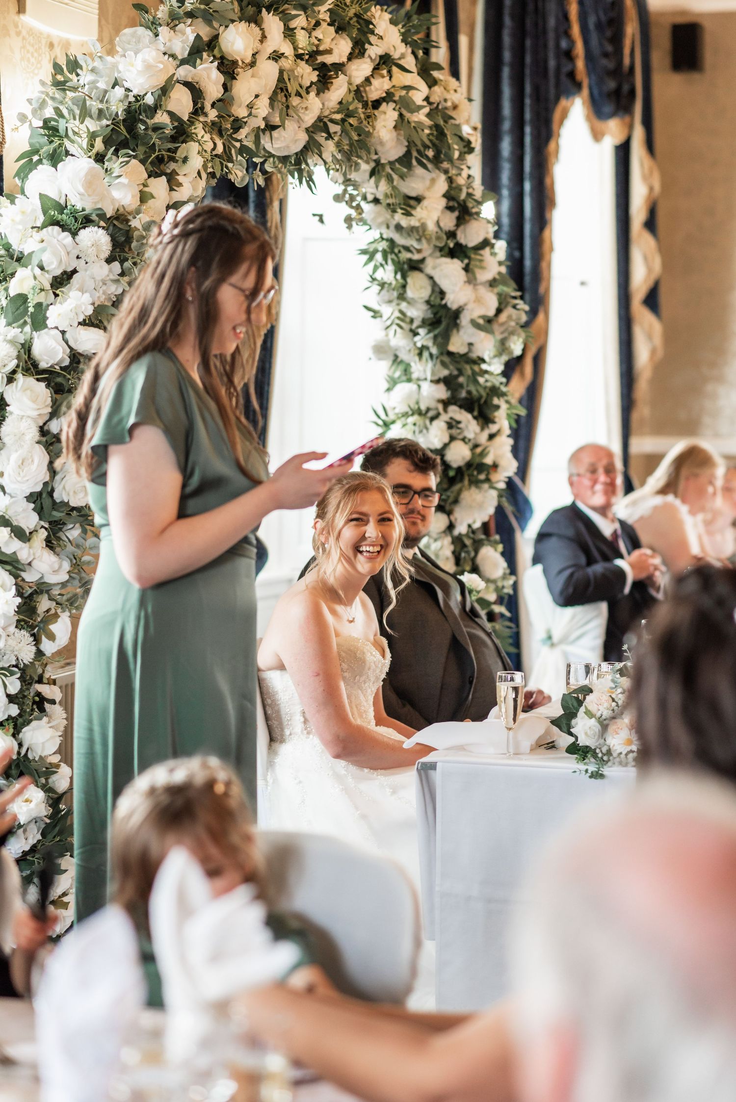 Wedding reception celebration under floral arch with elegant decor and seated guests.