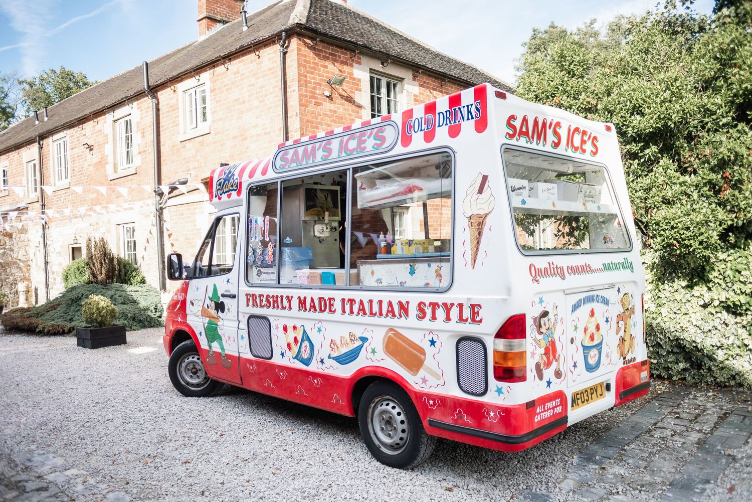 Vintage-style ice cream van decorated with red and blue stripes parked outside a brick building.
