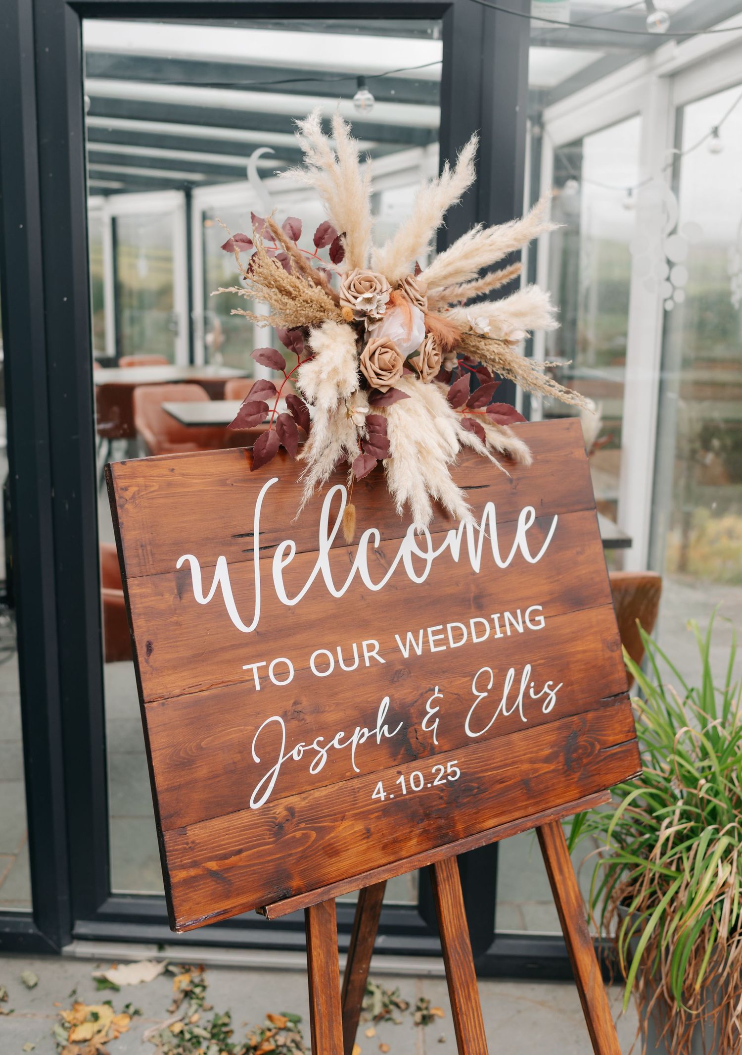 Rustic wooden wedding welcome signs decorated with dried flowers and white calligraphy displayed at an outdoor venue.
