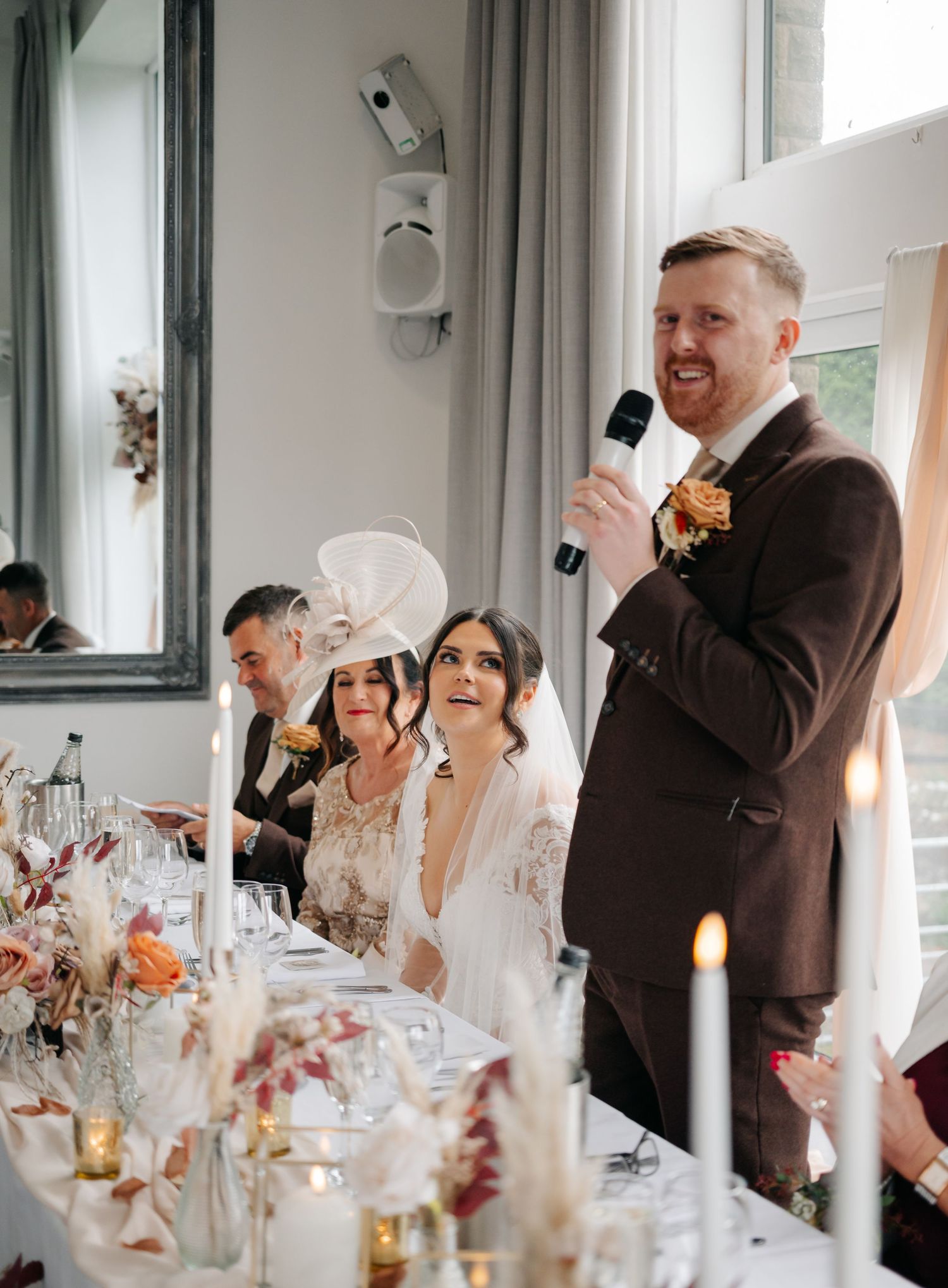 Wedding reception guests laugh and celebrate at elegantly set tables with candlelight and floral centerpieces.