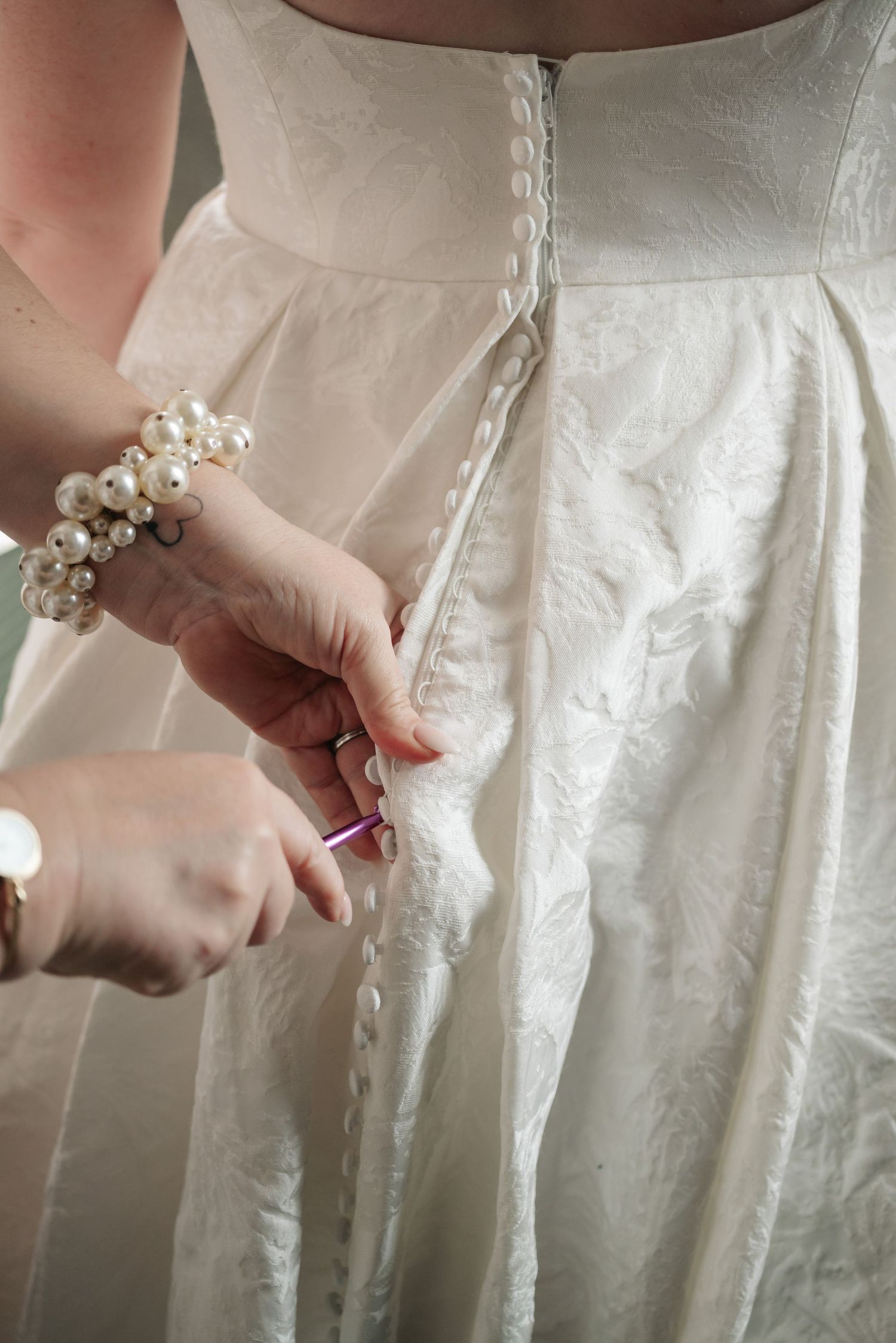Close-up details of delicate white wedding dress buttons and fabric textures.