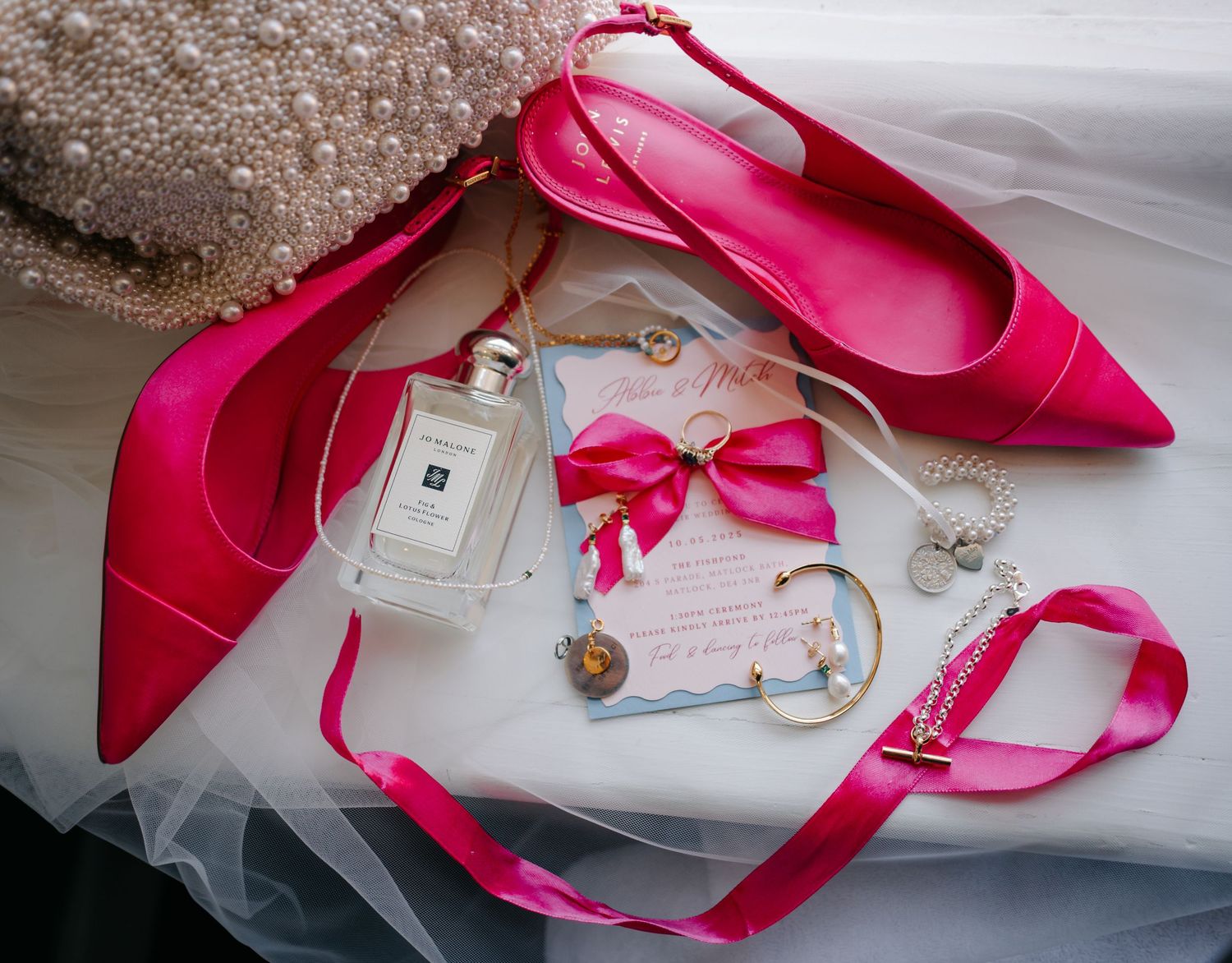 Hot pink satin high heel shoes arranged with delicate white tulle fabric and decorative ribbons.