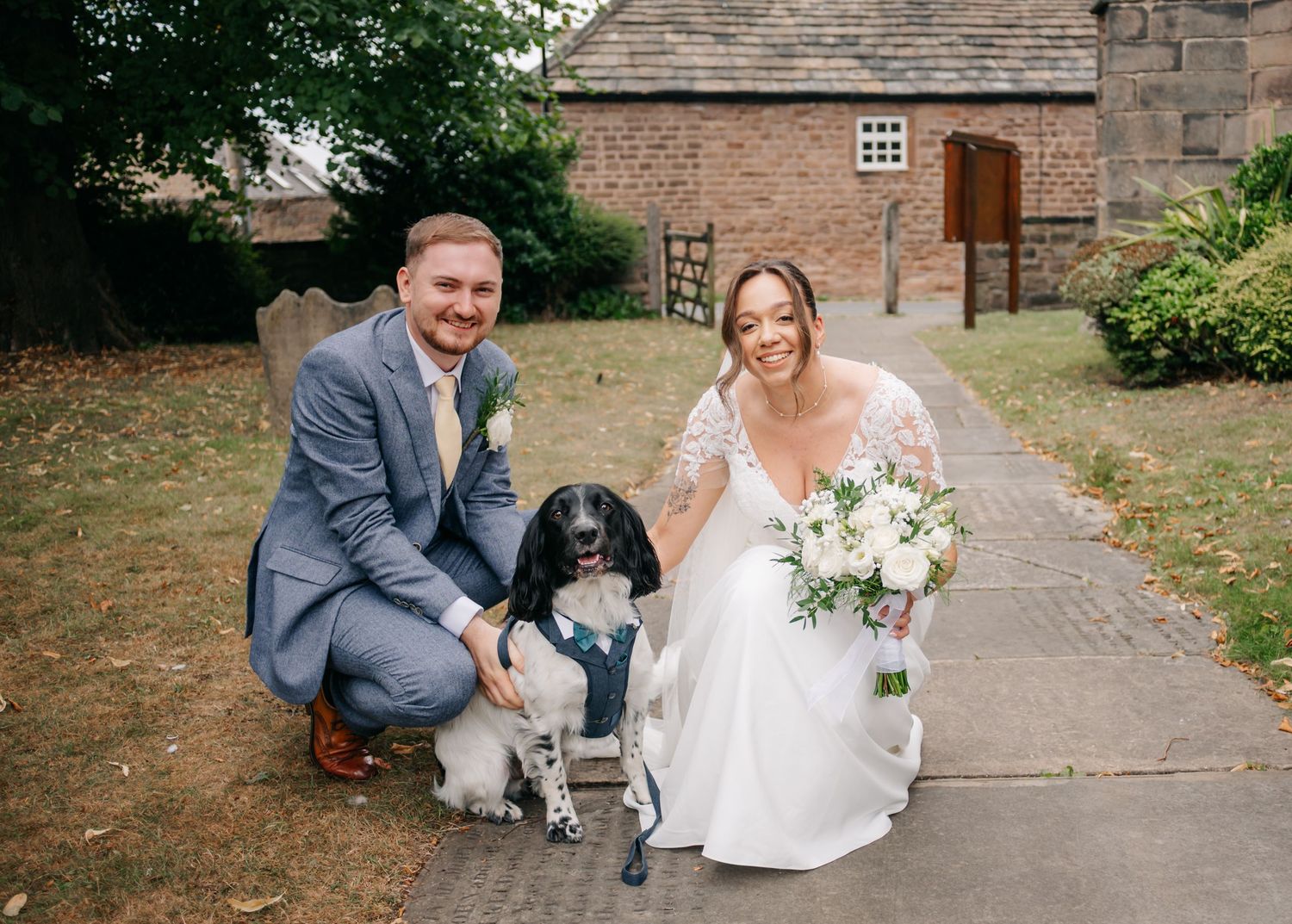 Wedding party posing outside historic church building with stone pathway.