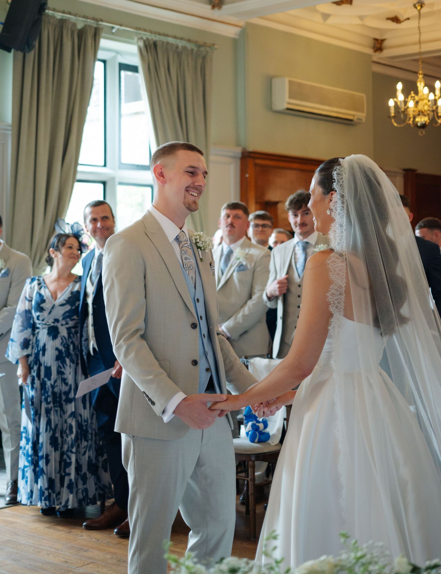 Wedding ceremony in an elegant room with light gray suits and white decor.