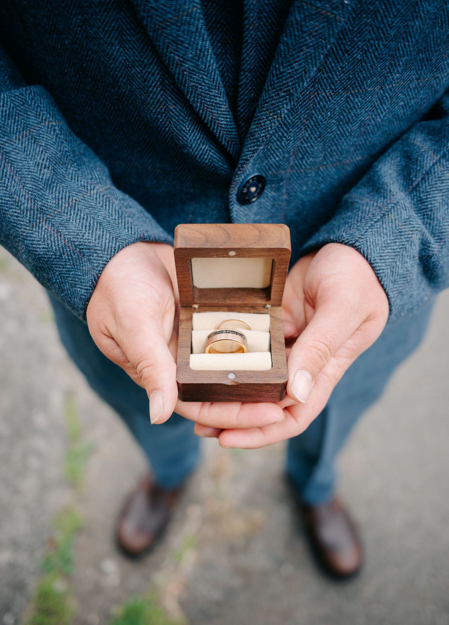 A series of hands holding small wooden ring boxes against a dark blue background.