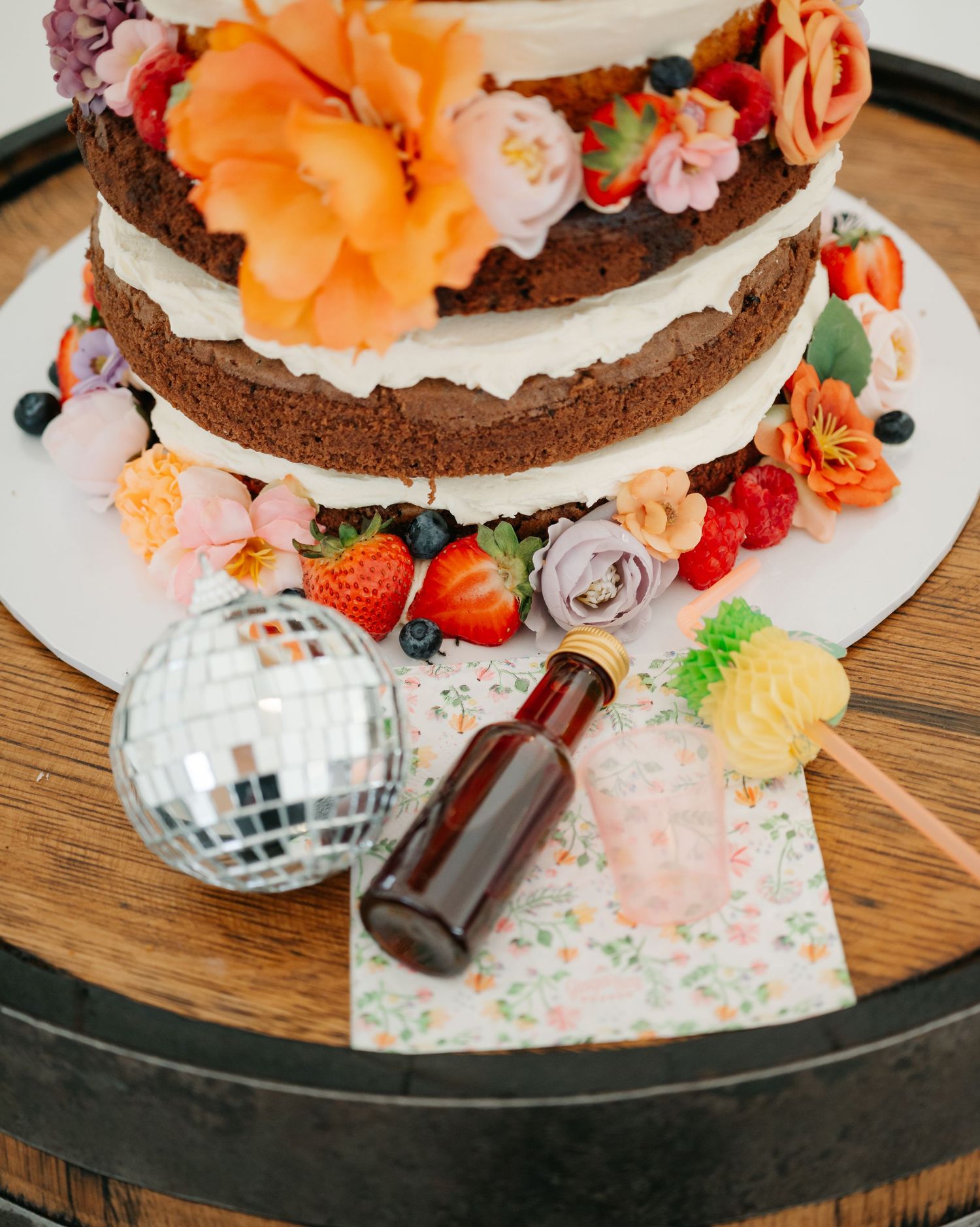 Chocolate layer cake decorated with fresh flowers, berries and disco ball decorations on a wooden table.