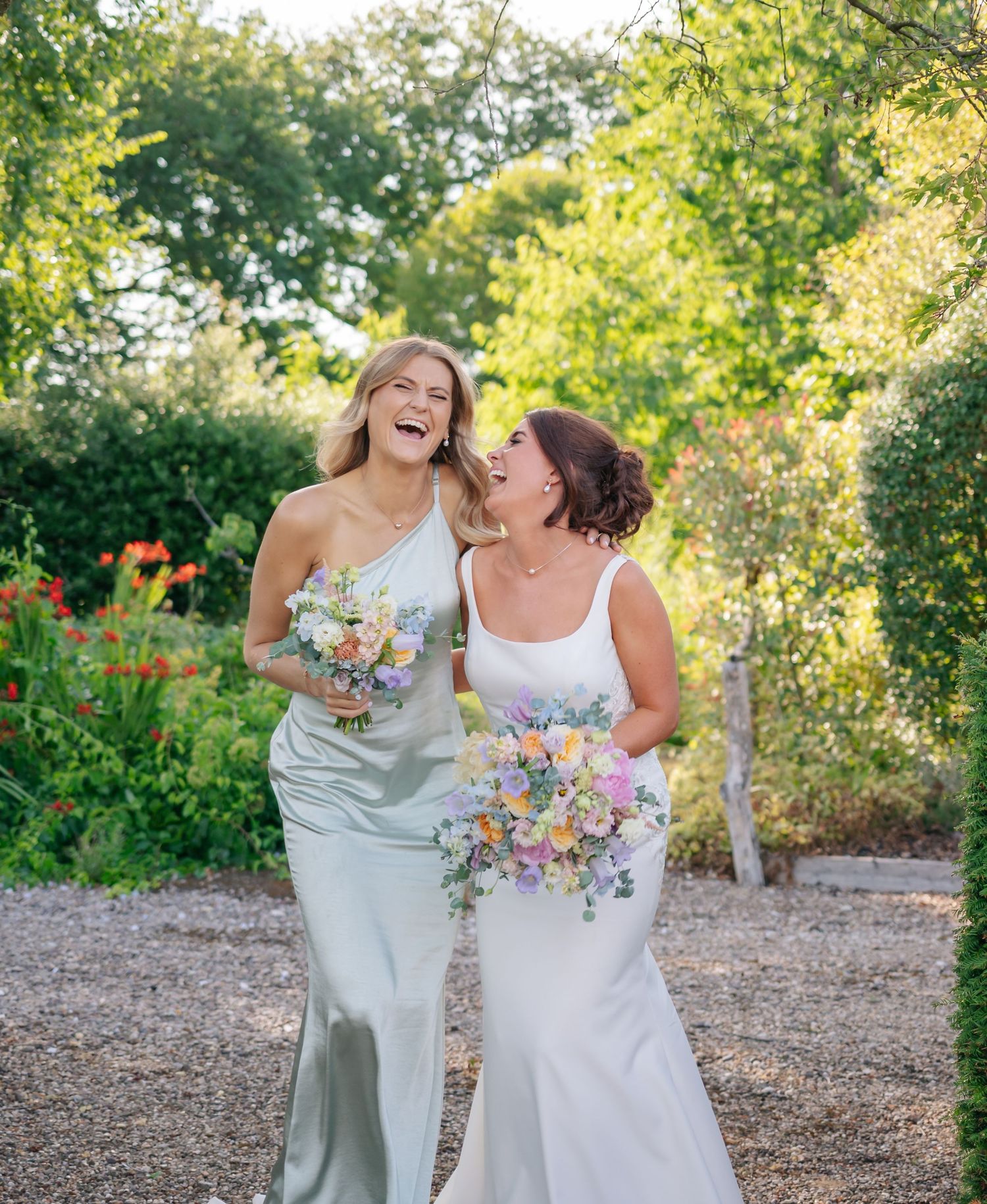 Wedding party sharing joyful laughter together in a sunlit garden setting.