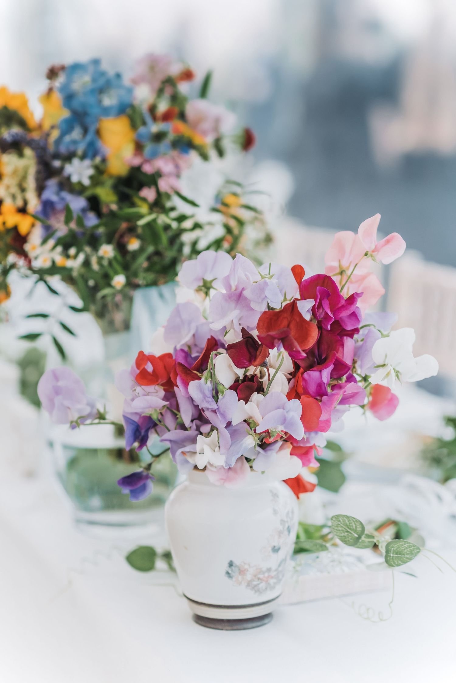 Colorful sweet pea and wildflower arrangements in white vases on wedding table.