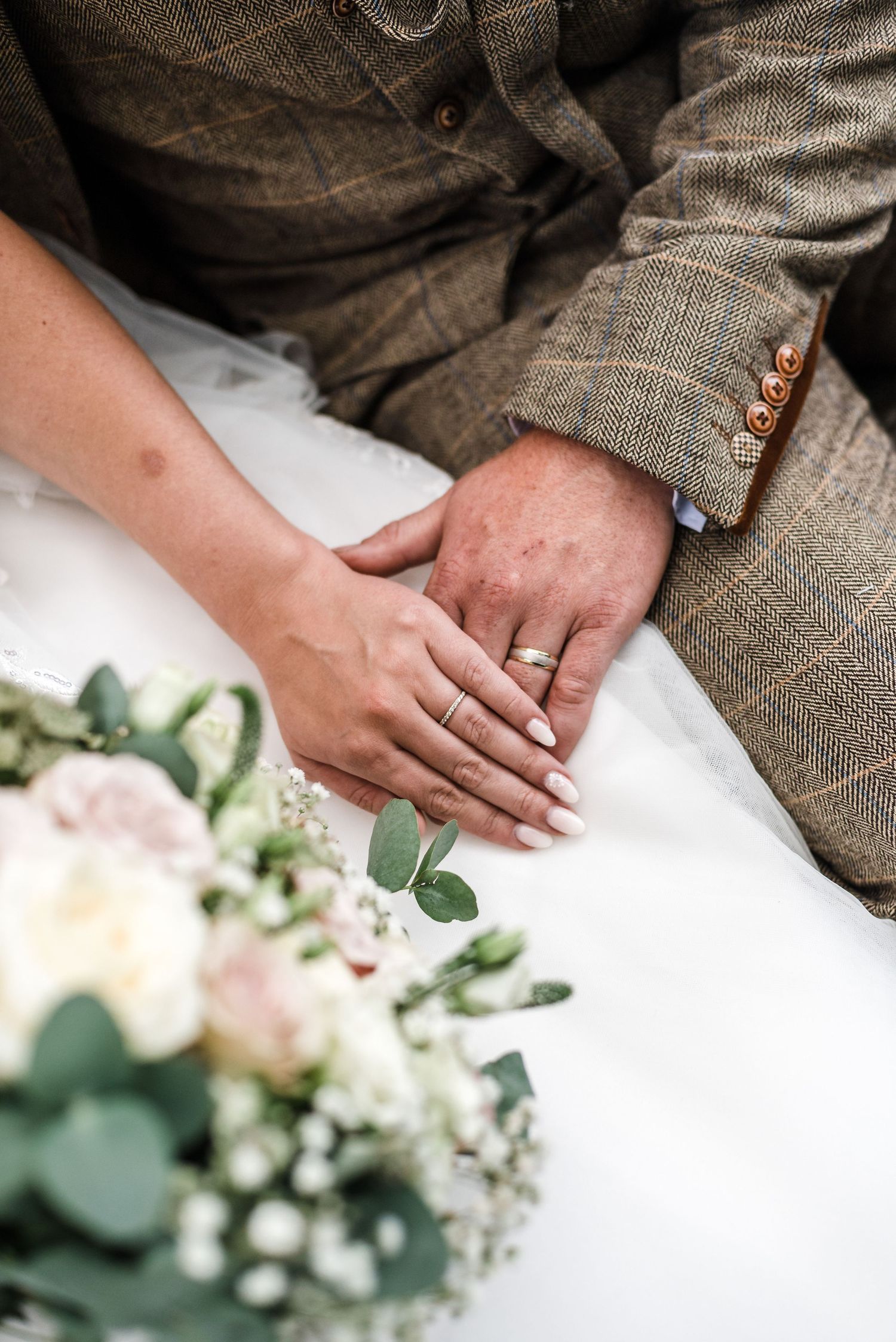Close-up of hands with wedding rings next to floral bouquet with eucalyptus.