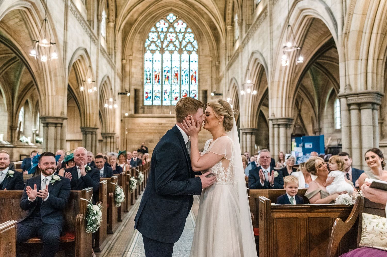 A couple sharing their first kiss during their wedding ceremony in a grand cathedral setting.