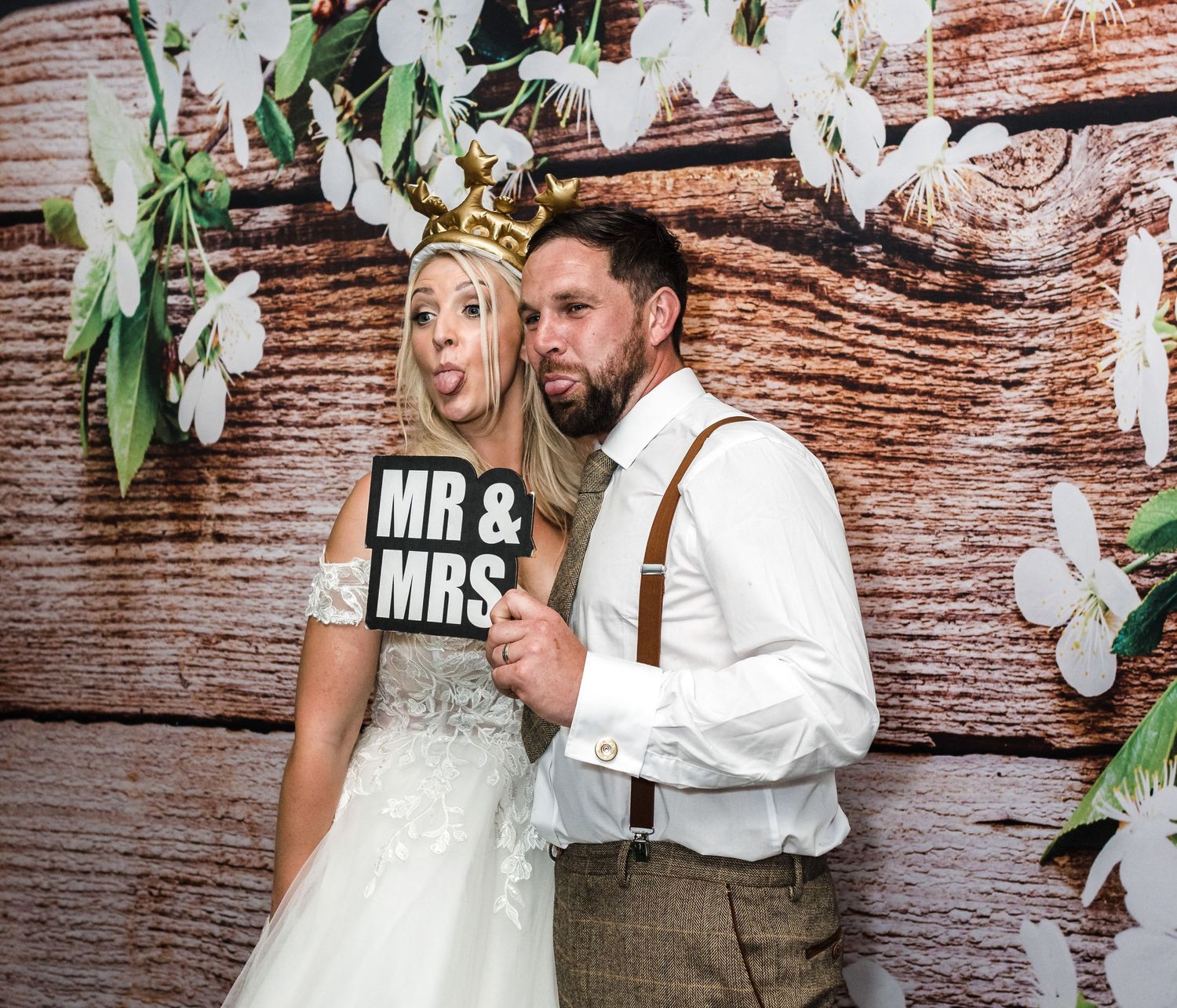 Couple poses with MR & MRS sign against rustic wooden wall with white orchid decorations.