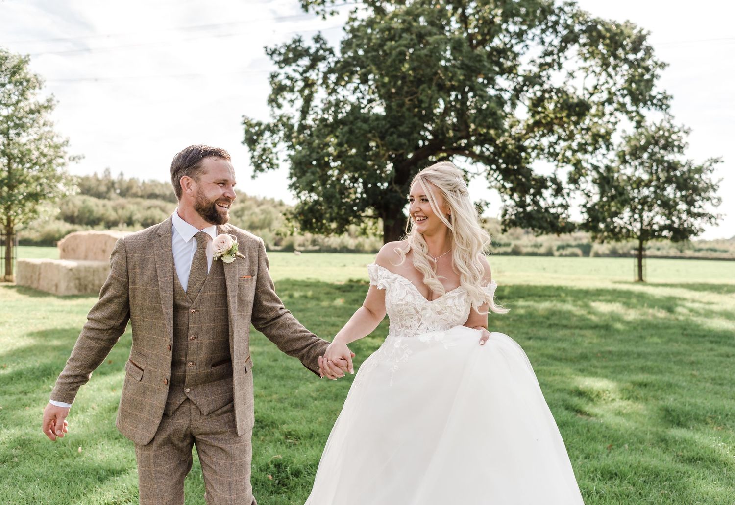 Couple walking and laughing together in a sunny field on their wedding day.