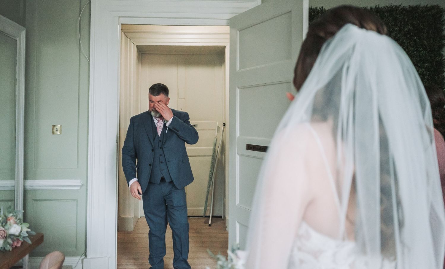 First look moment between couple in elegant sage green room with bride in veil.