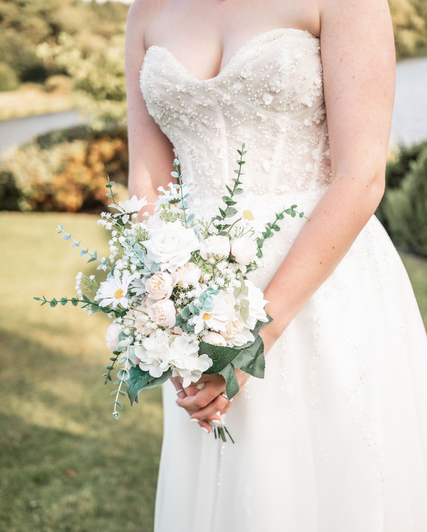 Close-up of bridal bouquet with white roses and greenery against wedding dress.