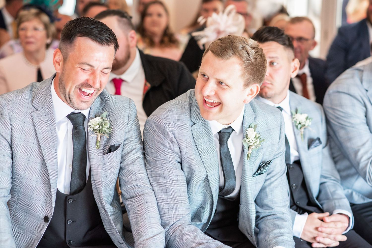 Wedding party enjoying a candid moment of laughter during a ceremony in matching gray suits.
