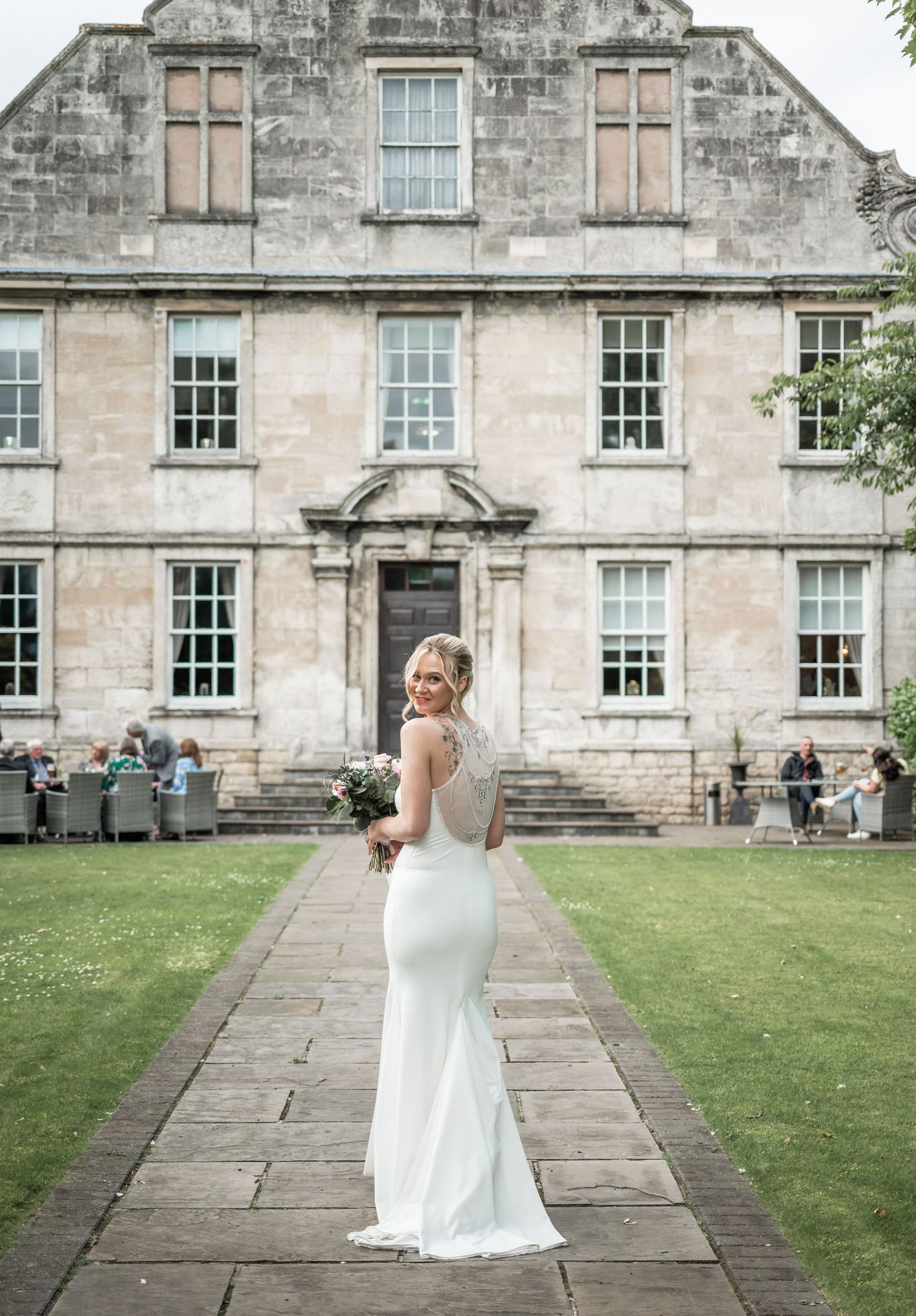 Bride in fitted white gown posing in front of historic stone building.