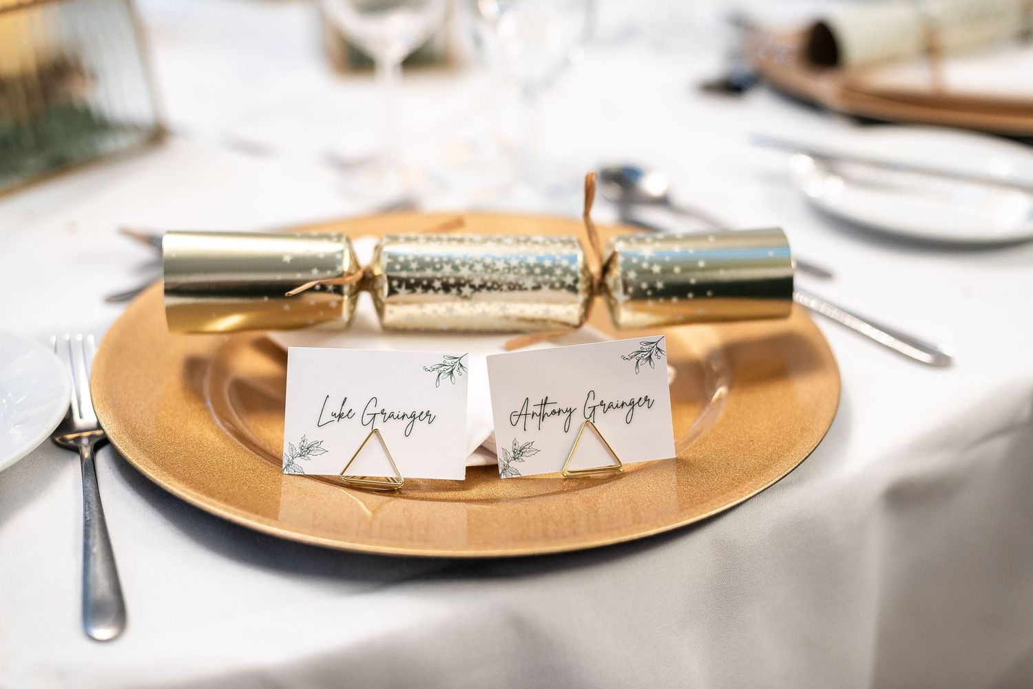 Gold Christmas cracker and place cards arranged on elegant table setting at formal event.