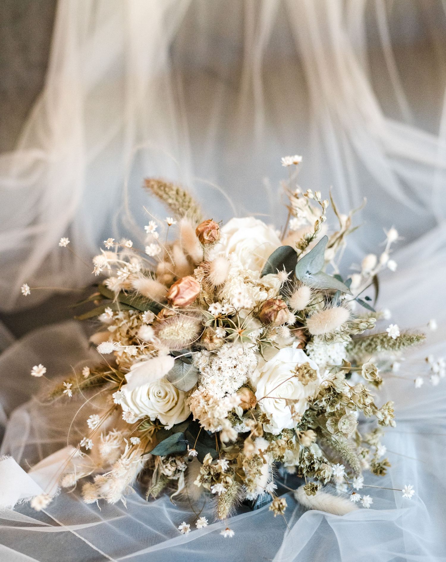 Romantic white and cream bridal bouquet with roses and dried flowers on tulle fabric.