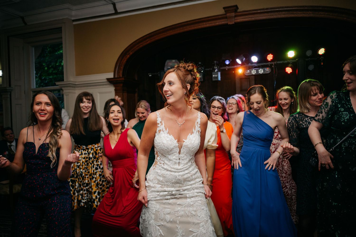 Wedding party celebrating on a dance floor with colorful stage lights and formal attire.