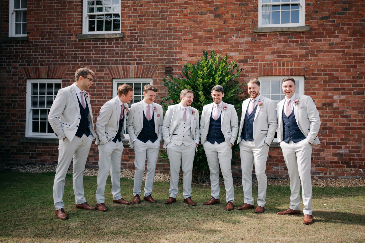 Groomsmen in light gray suits pose playfully against a brick wall in a creative series of mirrored shots.