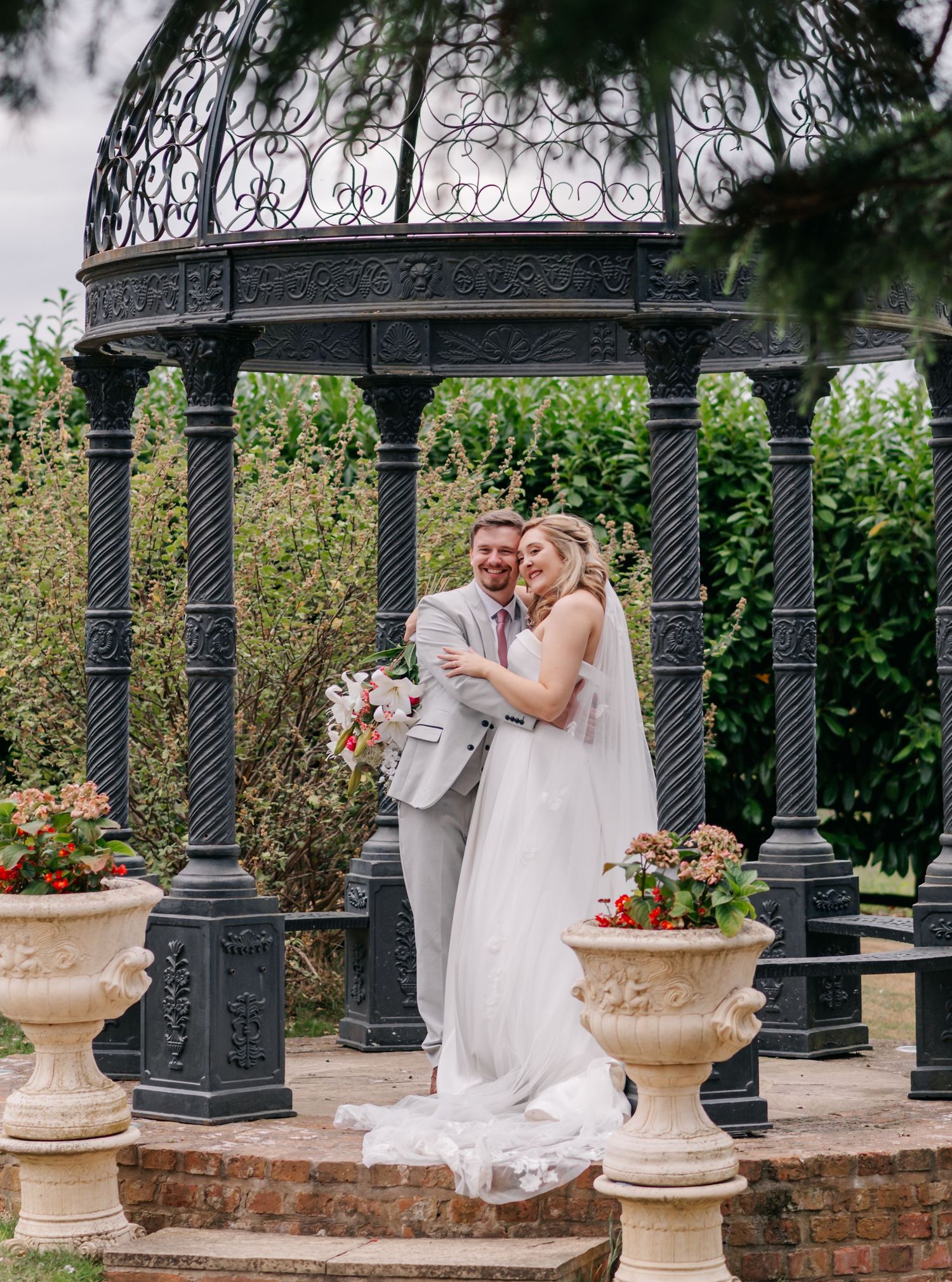 Romantic moment captured under a decorative iron gazebo with garden planters and greenery.