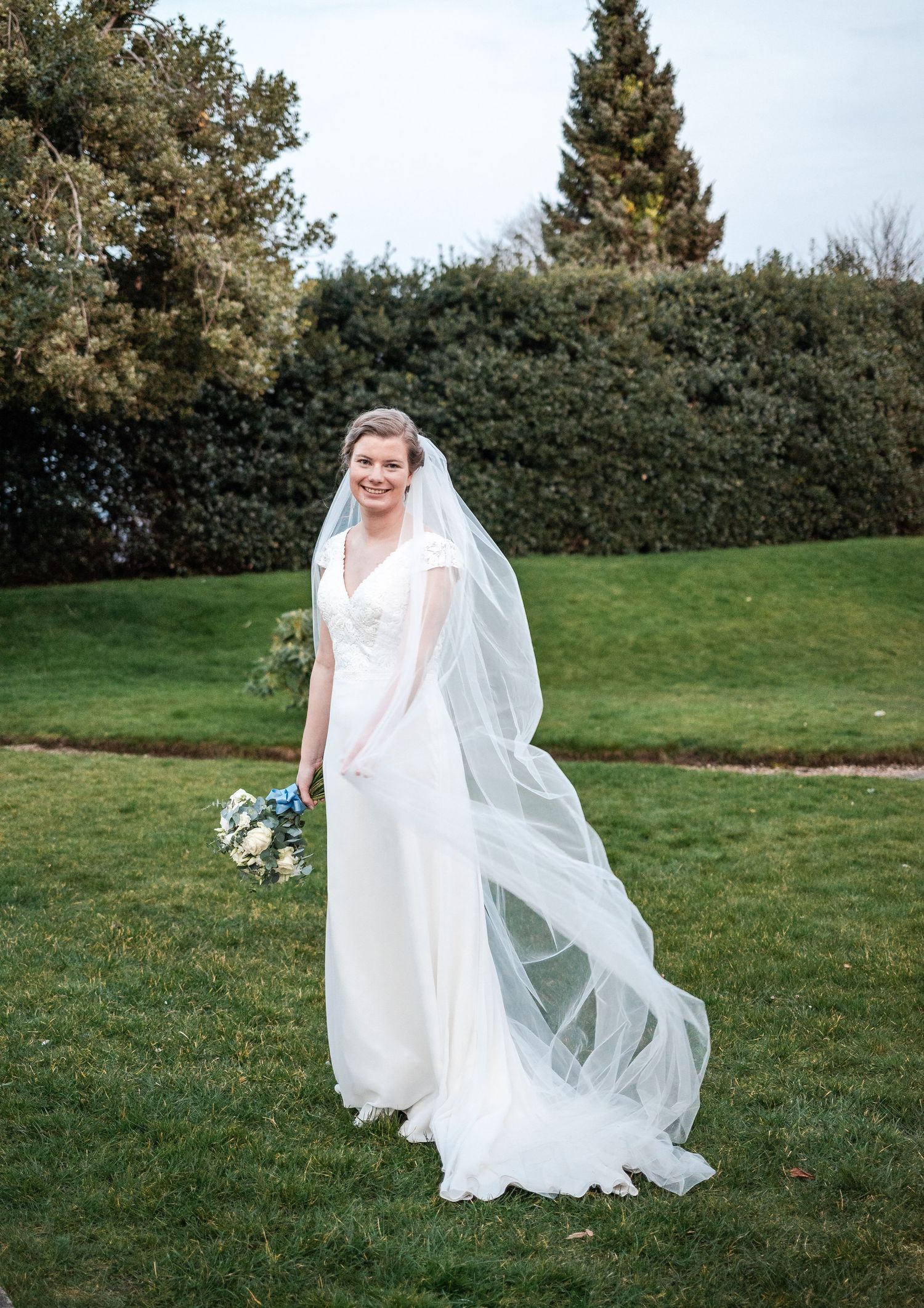 A flowing white wedding dress and veil catch the breeze in a series of outdoor photos on a grassy lawn.
