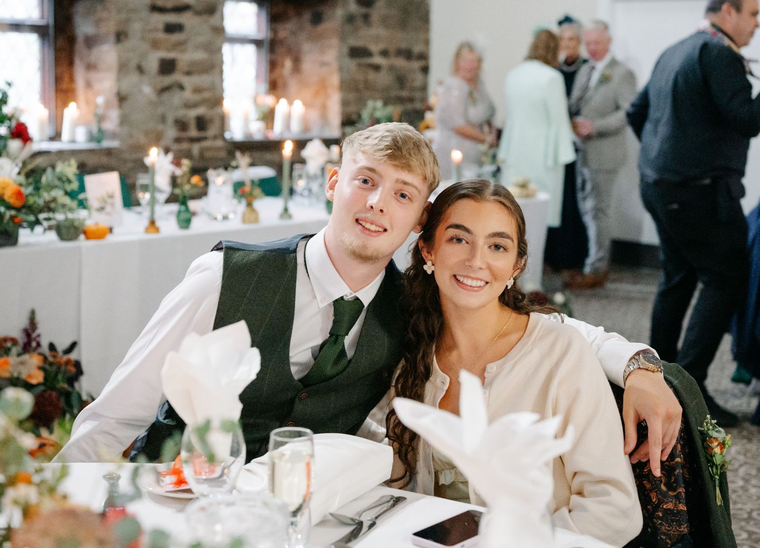 Wedding reception guests seated at decorated tables in rustic stone venue.