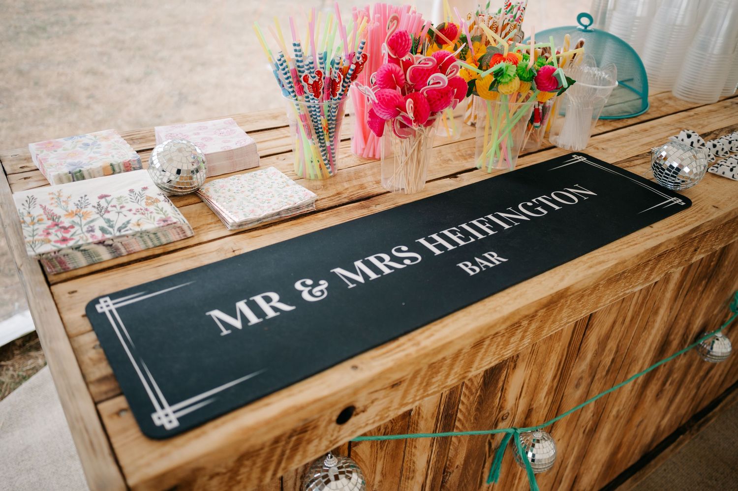 A wooden table displays a black personalized 'Mr & Mrs' sign with colorful flowers in rustic wooden boxes.