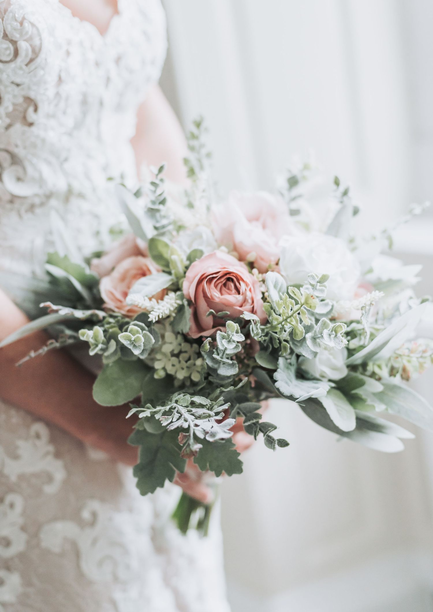 A delicate bridal bouquet featuring blush roses and eucalyptus leaves against a white lace dress.