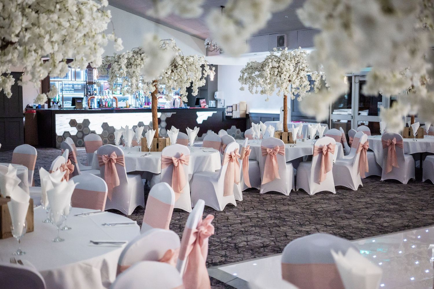 Elegant wedding reception venue decorated with white chair covers, pink bows and hanging floral arrangements.