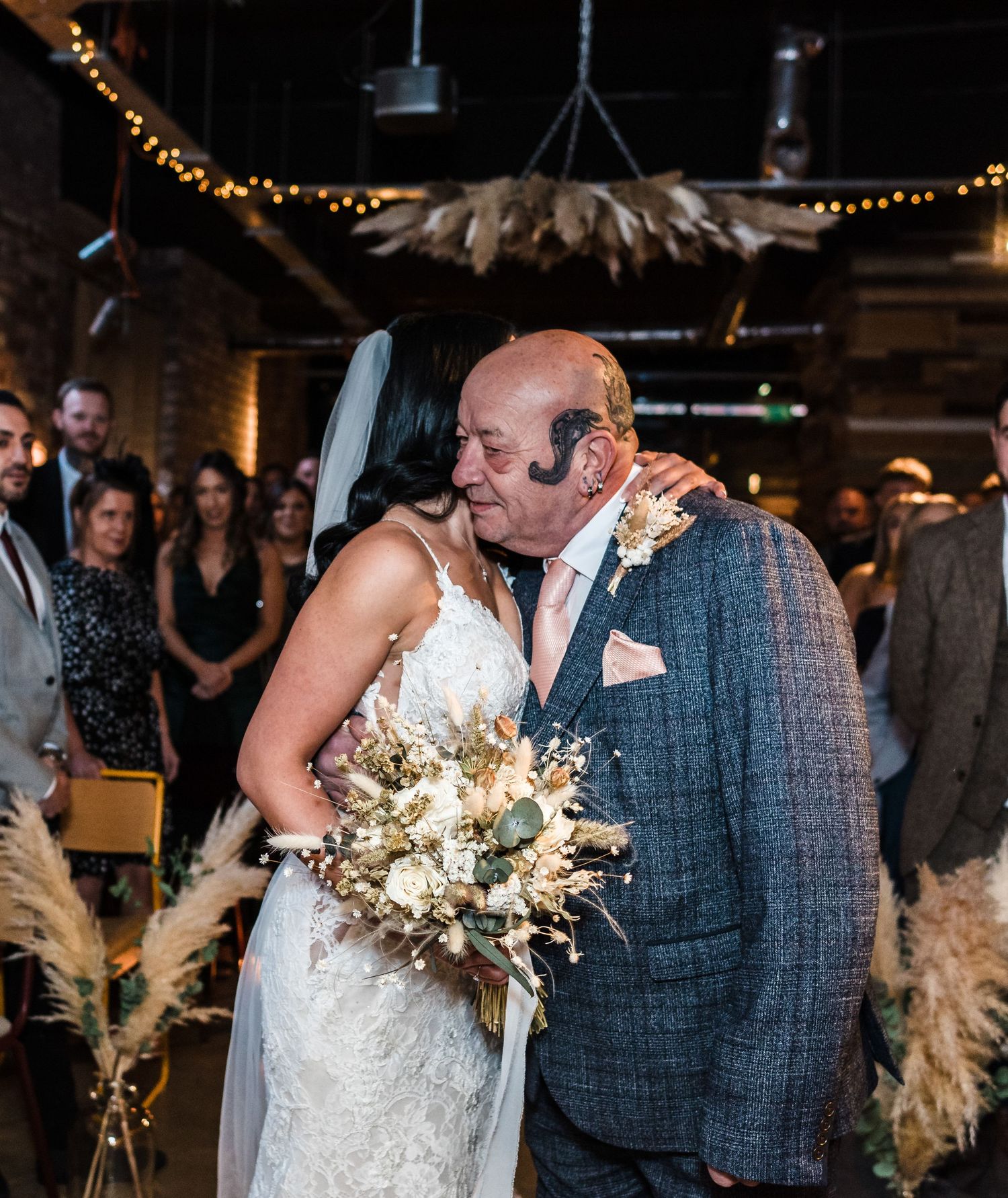 Emotional father-daughter moment during wedding ceremony in rustic venue with string lights.