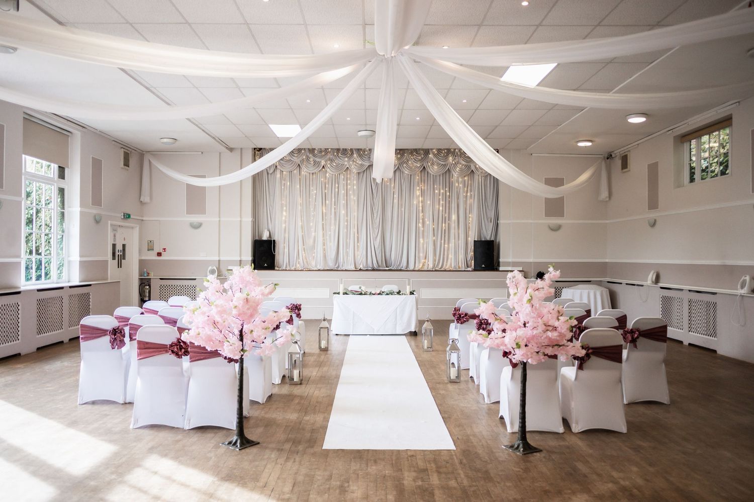 Elegant white wedding ceremony room decorated with pink floral arrangements and draped fabric ceiling.