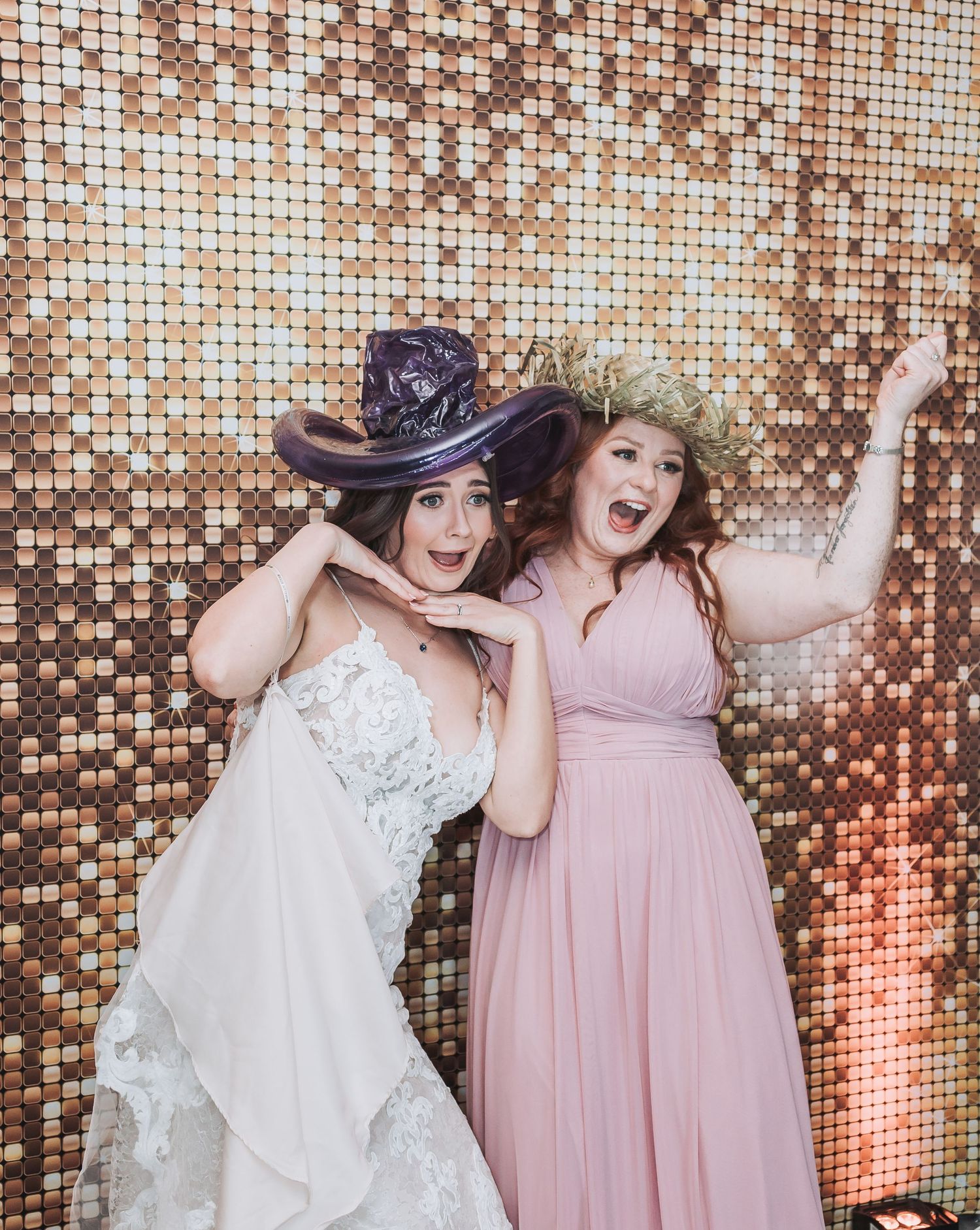 Two people posing playfully against a sparkly gold sequin backdrop at a wedding.