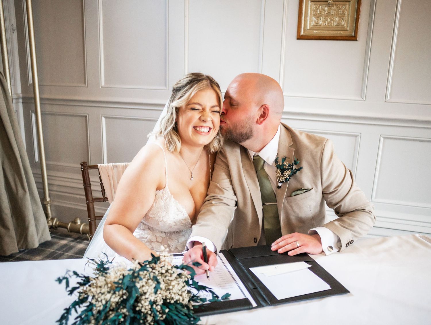 Intimate moment captured during wedding document signing in an elegant white room.