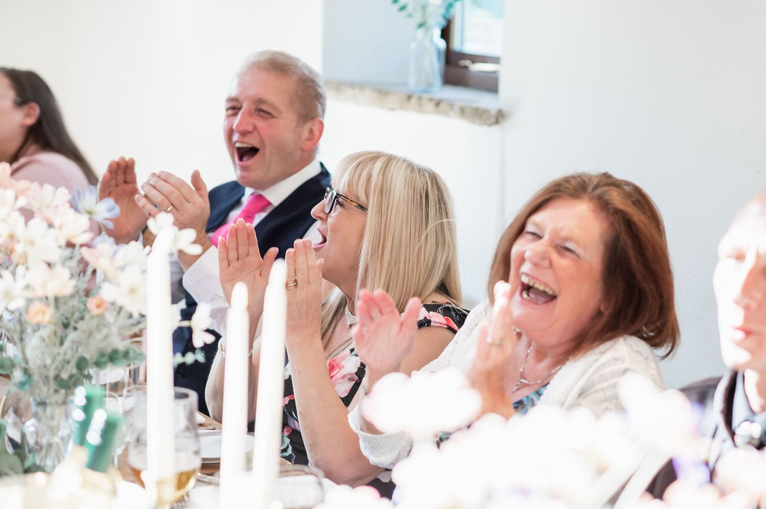 Wedding guests laugh and clap with enthusiasm during reception celebrations.
