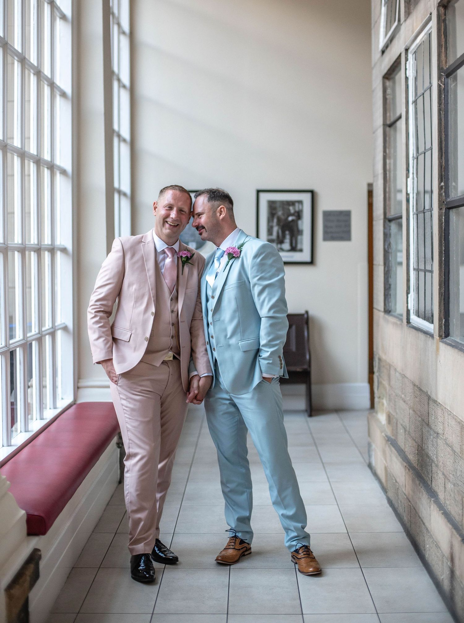 Two people in pastel suits sharing an intimate moment in a bright hallway.