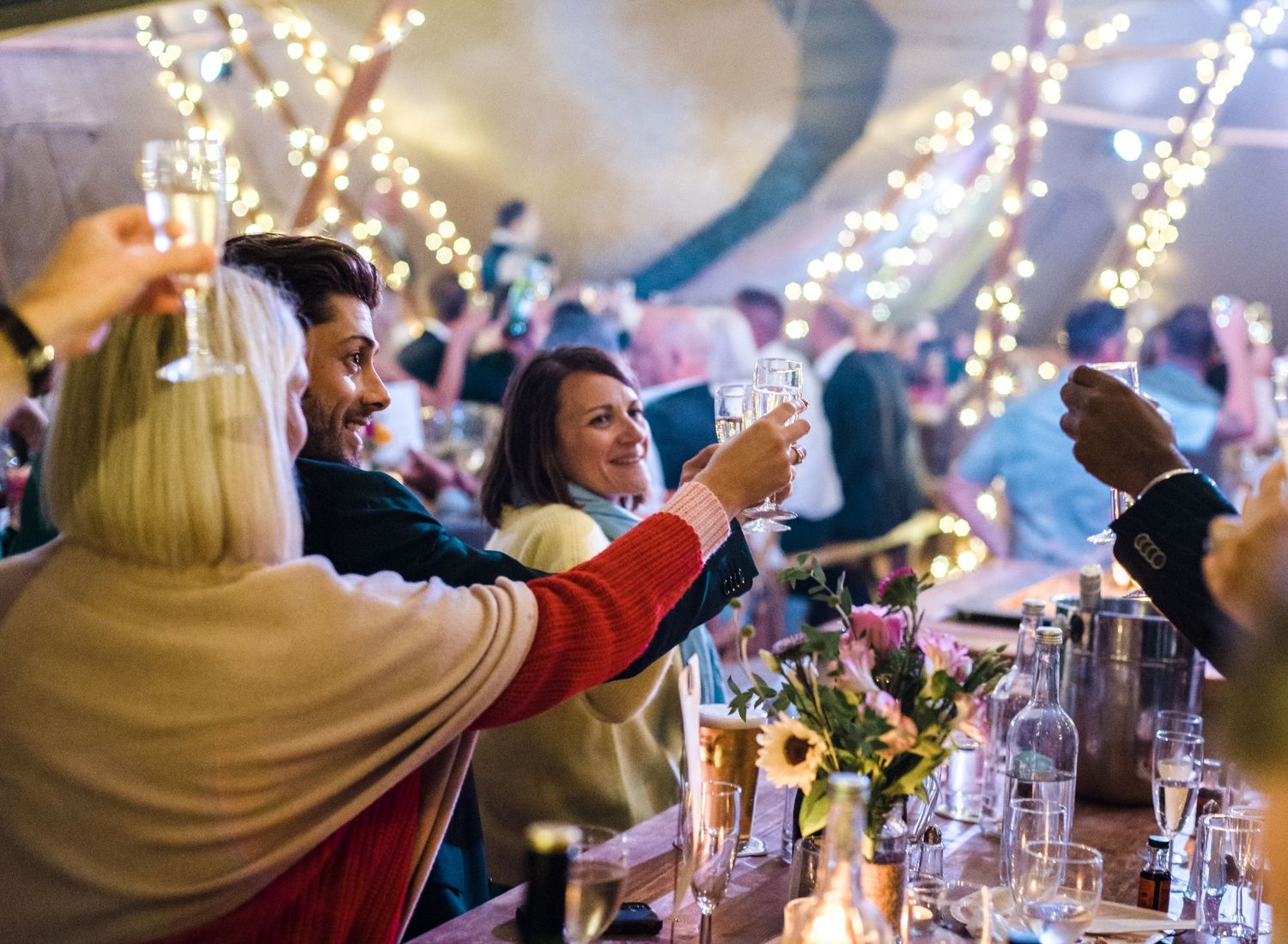 Guests toasting and celebrating at festively lit dinner table during reception.