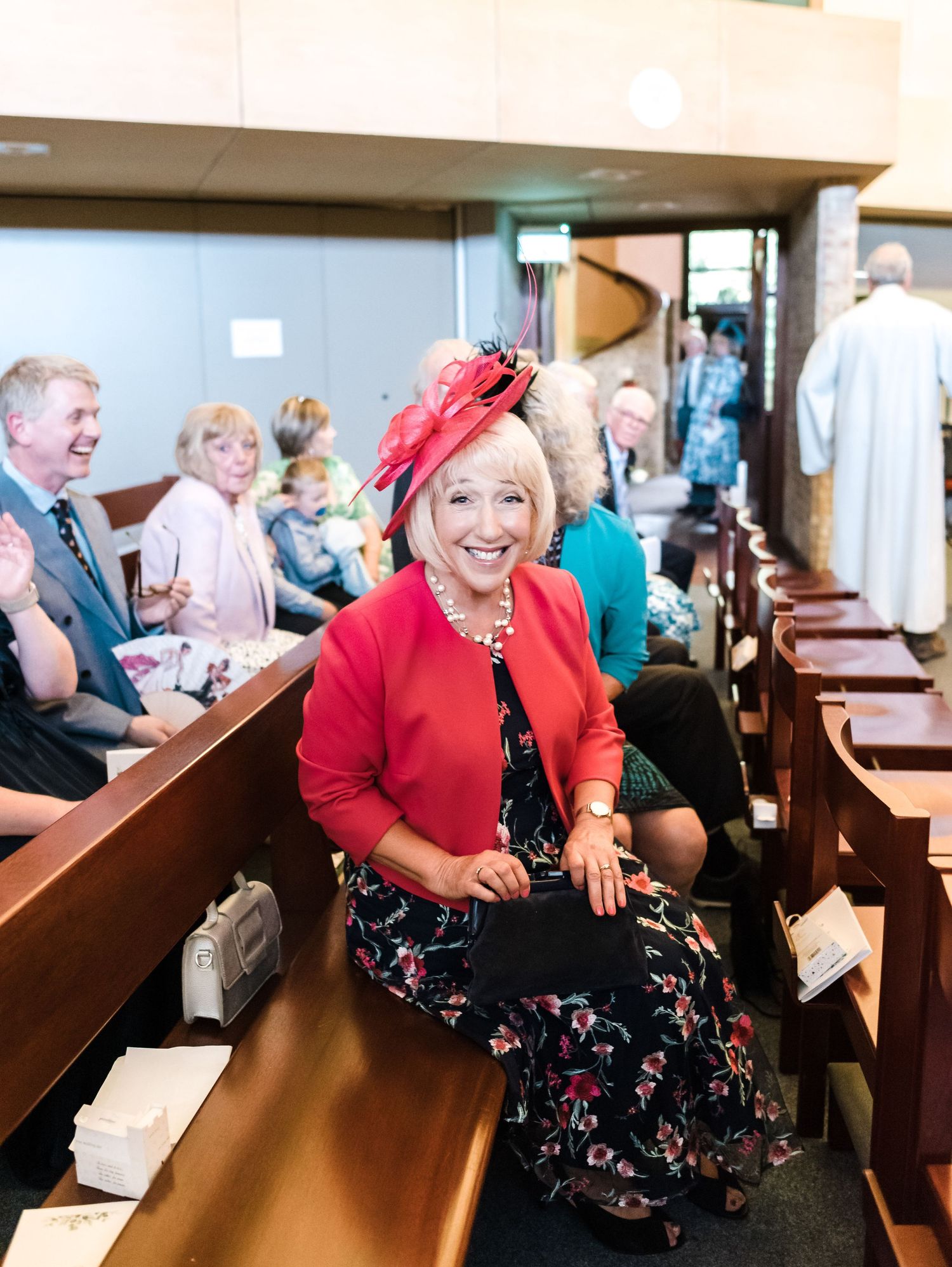 A woman in red attire sits in a church pew with festive decorations and floral patterns.