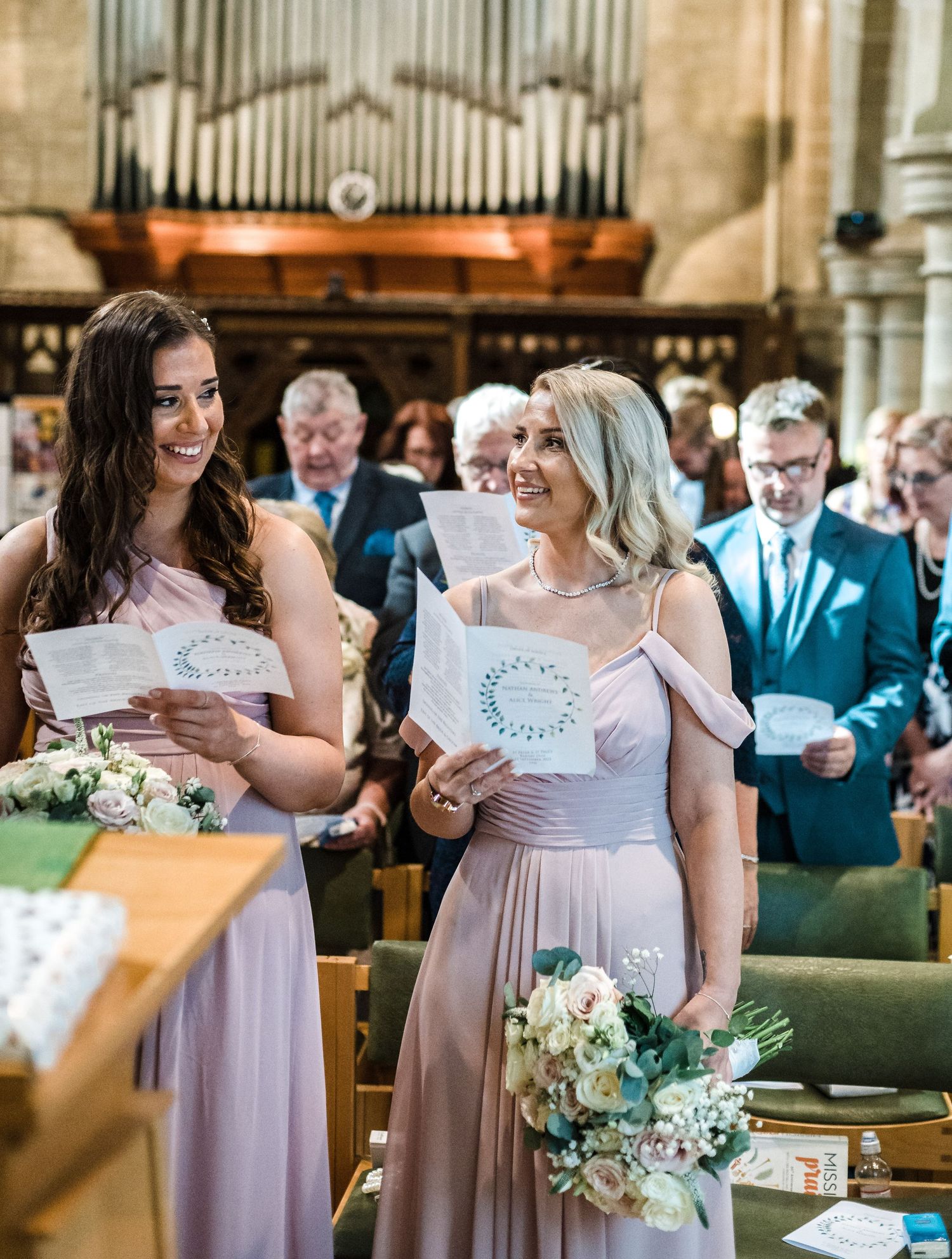 Wedding attendants in pink dresses holding ceremony programs in historic church.