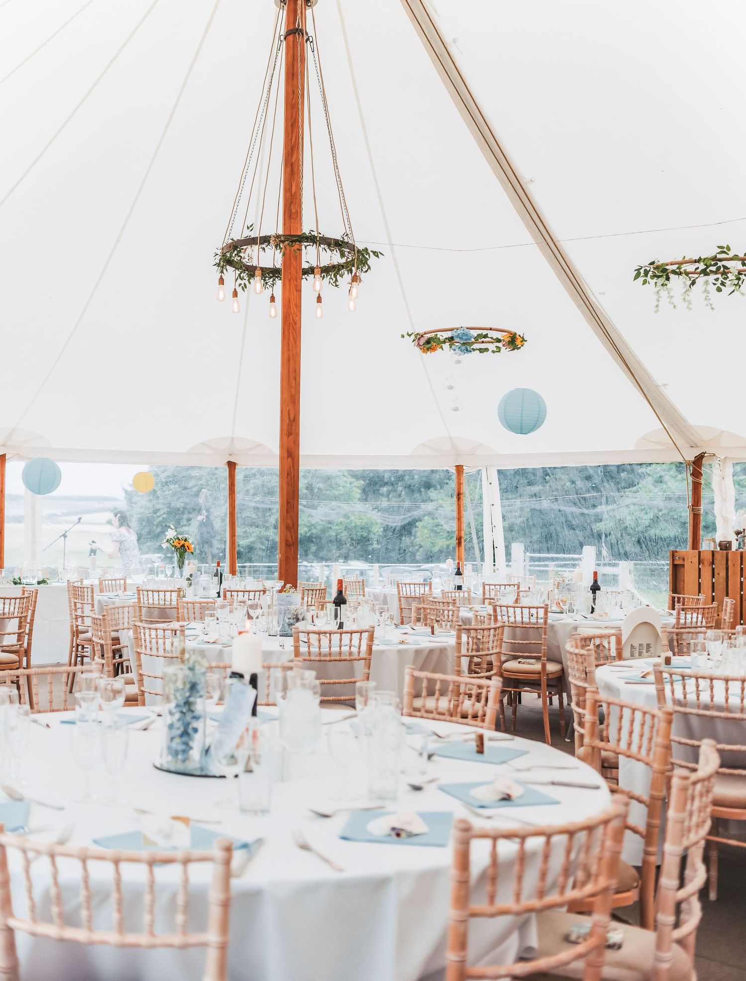 Elegant wedding reception setup in white tent with rustic chandelier and chiavari chairs.
