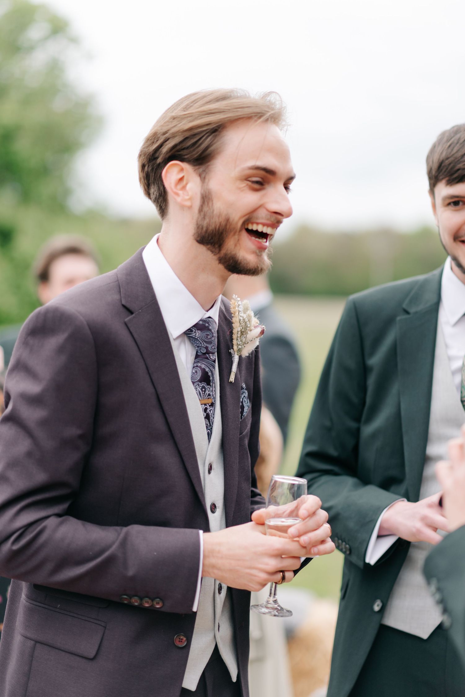 Groomsmen in formal suits sharing a candid moment and laughter outdoors.