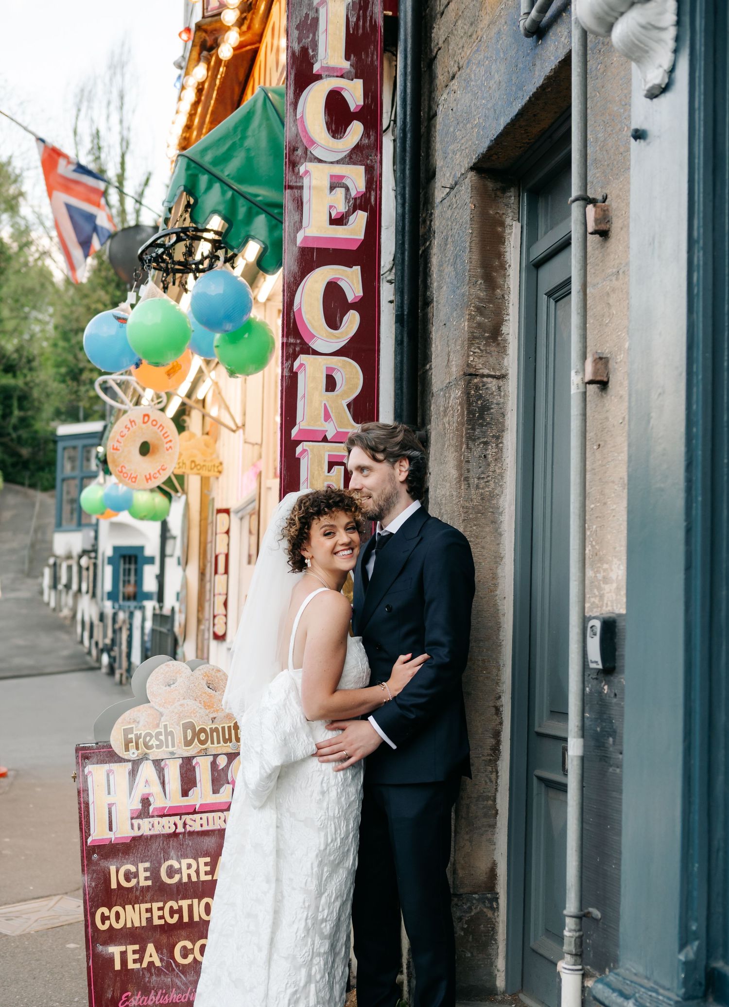 Wedding couple poses outside a vintage ice cream shop with colorful balloons.