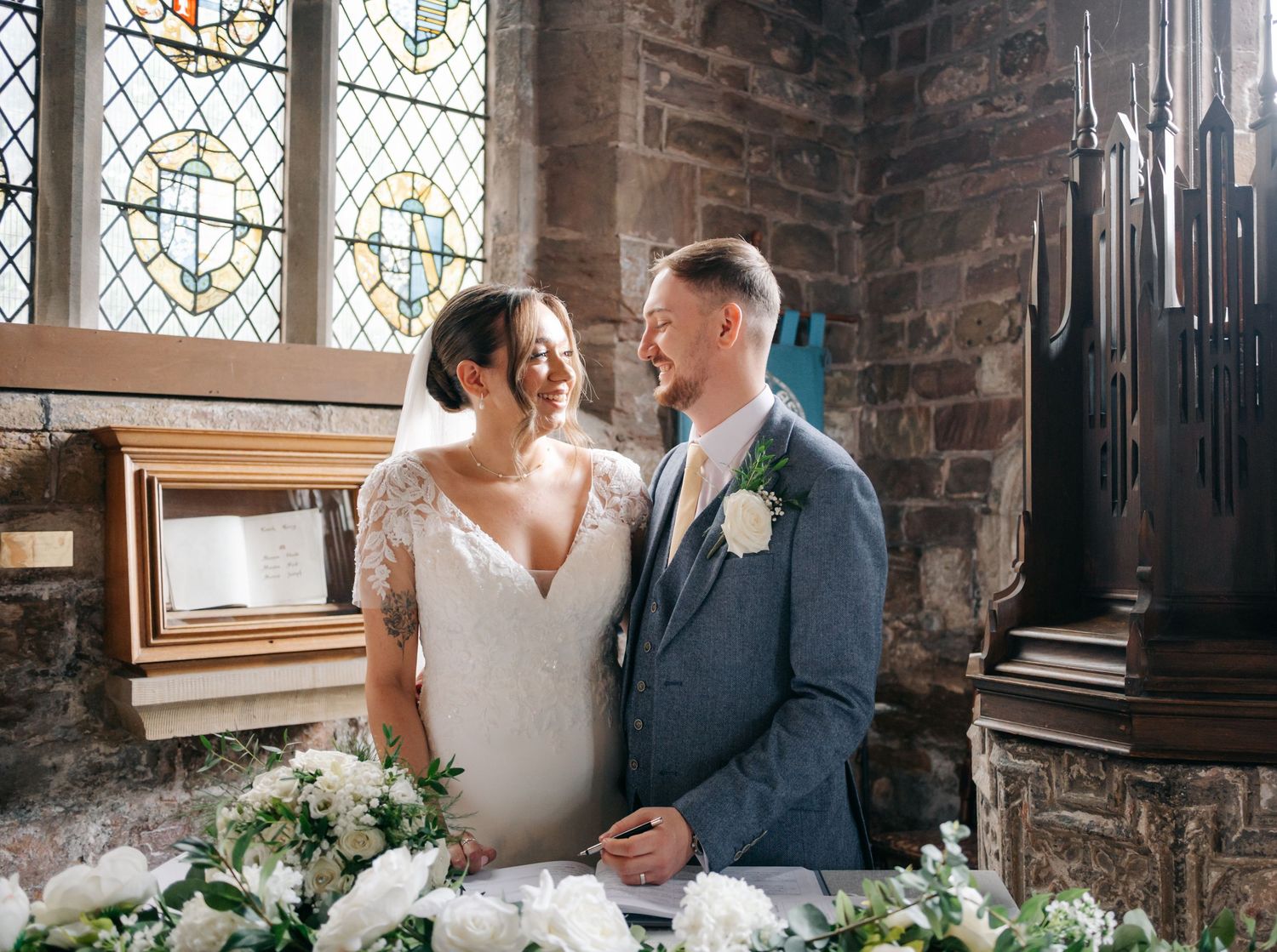 Stained glass windows illuminate a romantic moment in a stone church interior.