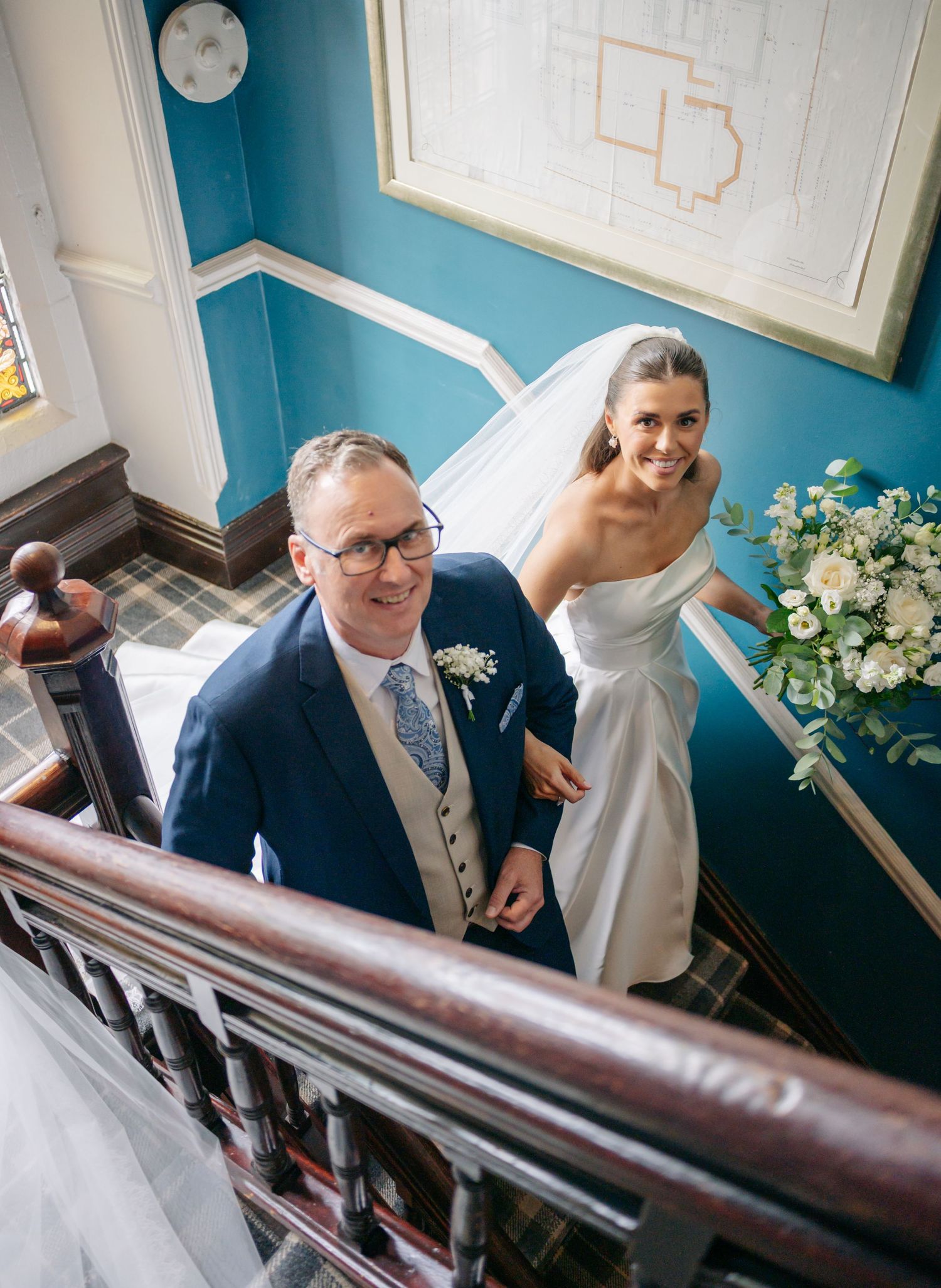 Wedding party members ascend a staircase with blue walls and wooden handrails.