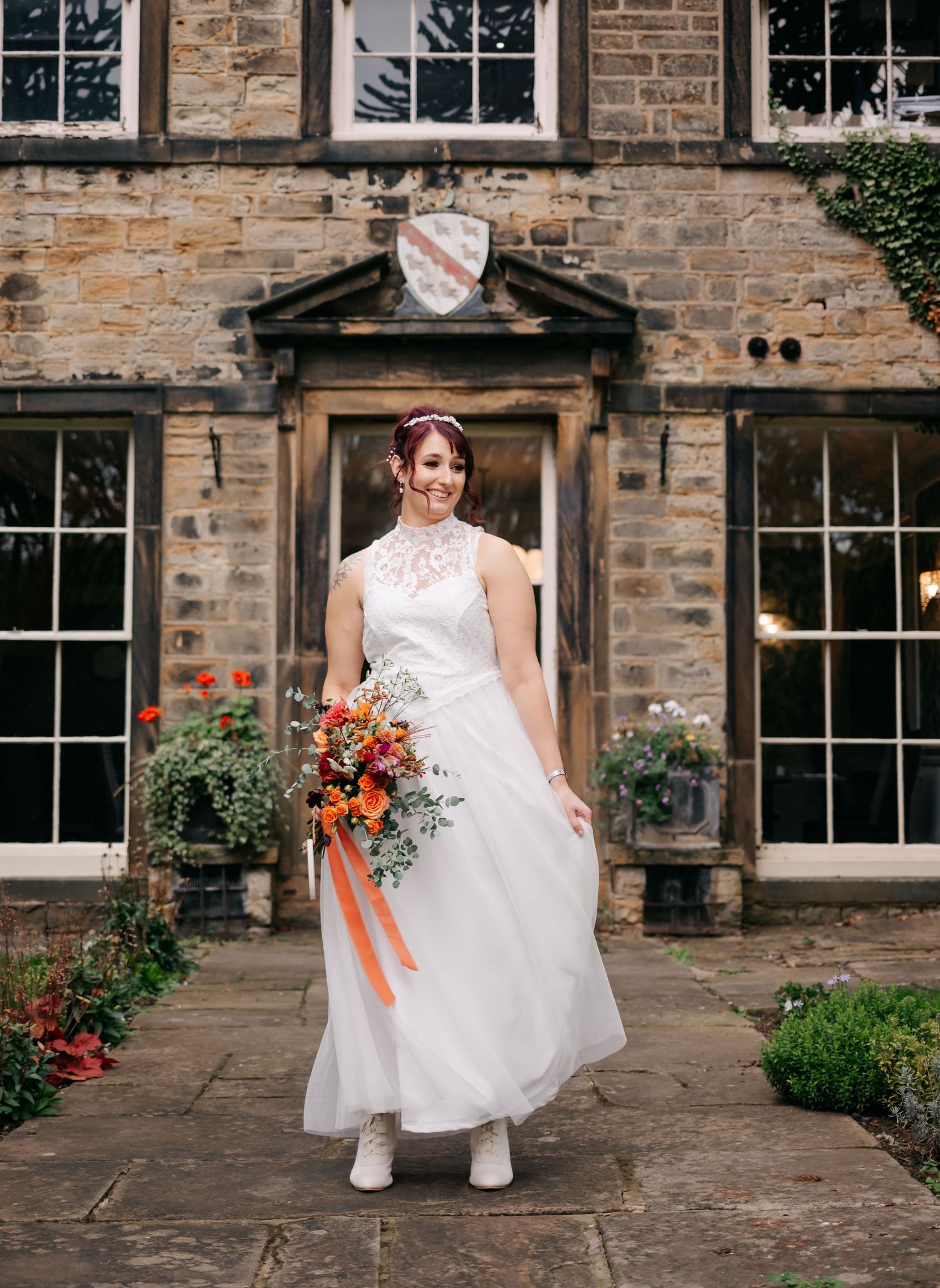 Bride in white lace dress posing on stone patio in front of historic building.