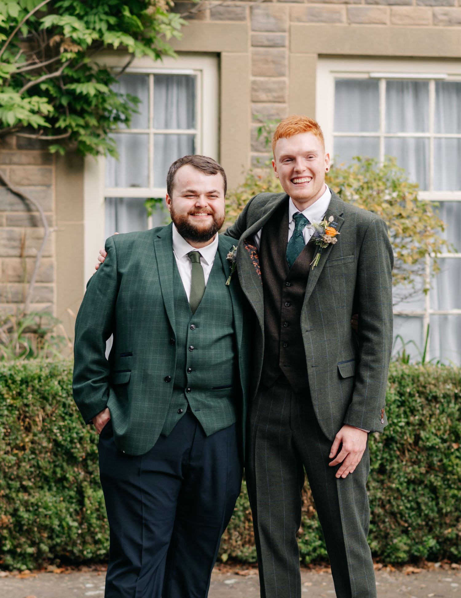 Groomsmen in dark suits standing together outside a stone building.