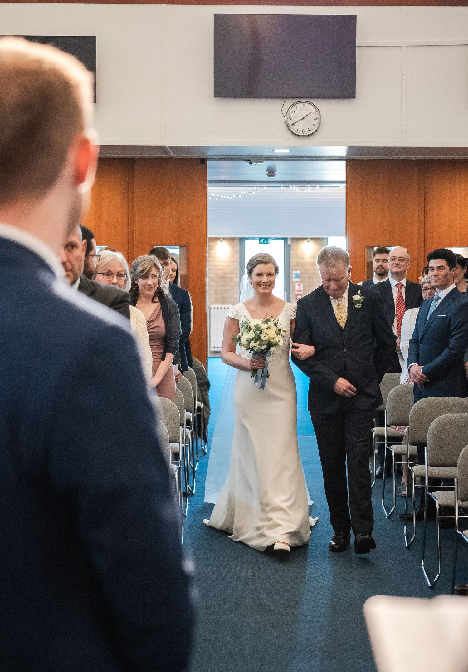 Wedding ceremony processional in a modern conference room with guests seated in rows.