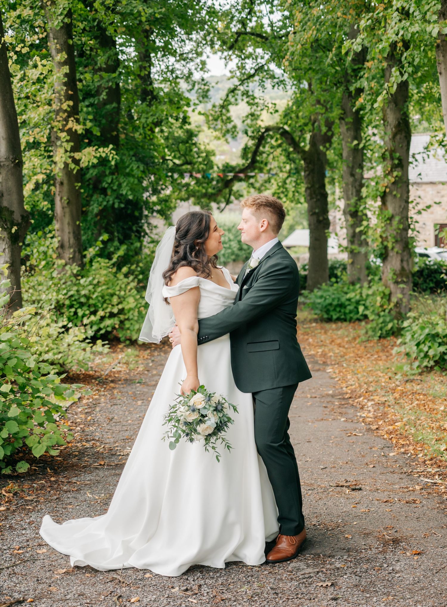 Romantic wedding couple shares intimate moments while walking along a tree-lined path.